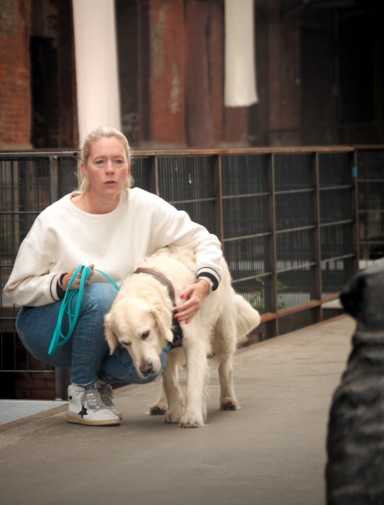 Frau kniet mit angeleintem Hund vor einer Hundestatue – Training zur kontrollierten Begegnungssituation in der RUDEL. App.