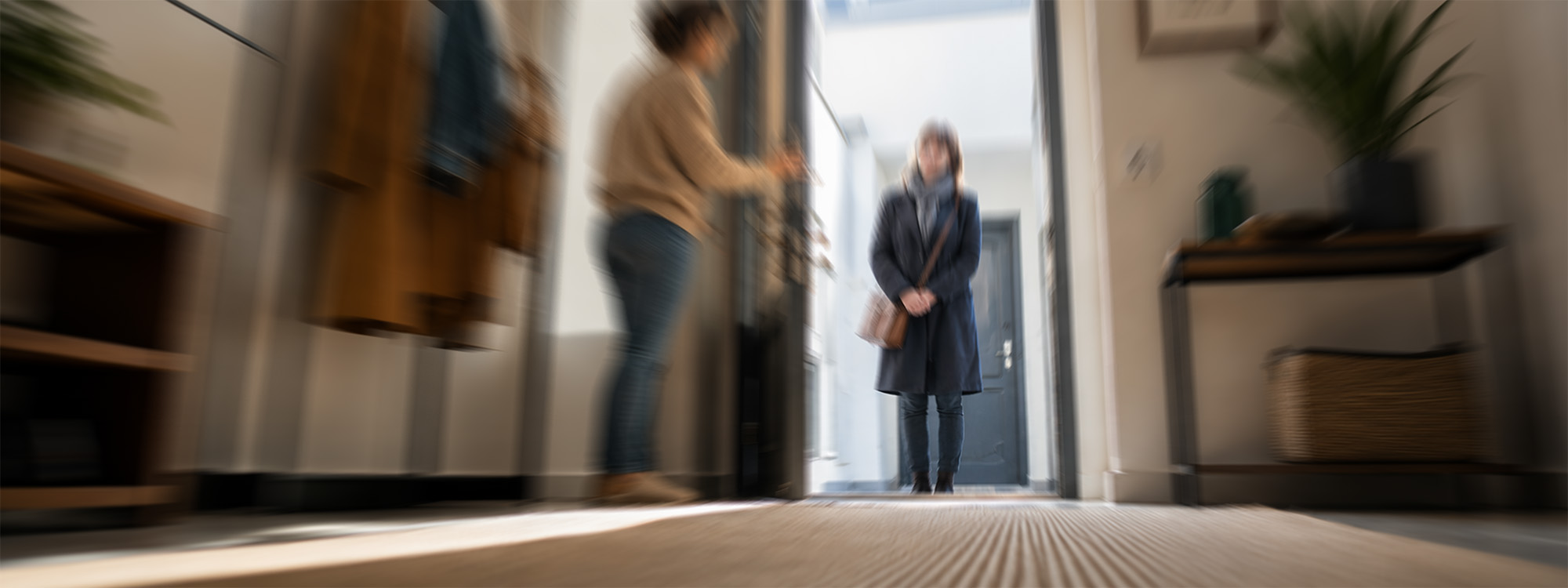 Frau macht Wohnungstür auf und begrüßt Besuch, Welpe nähert sich