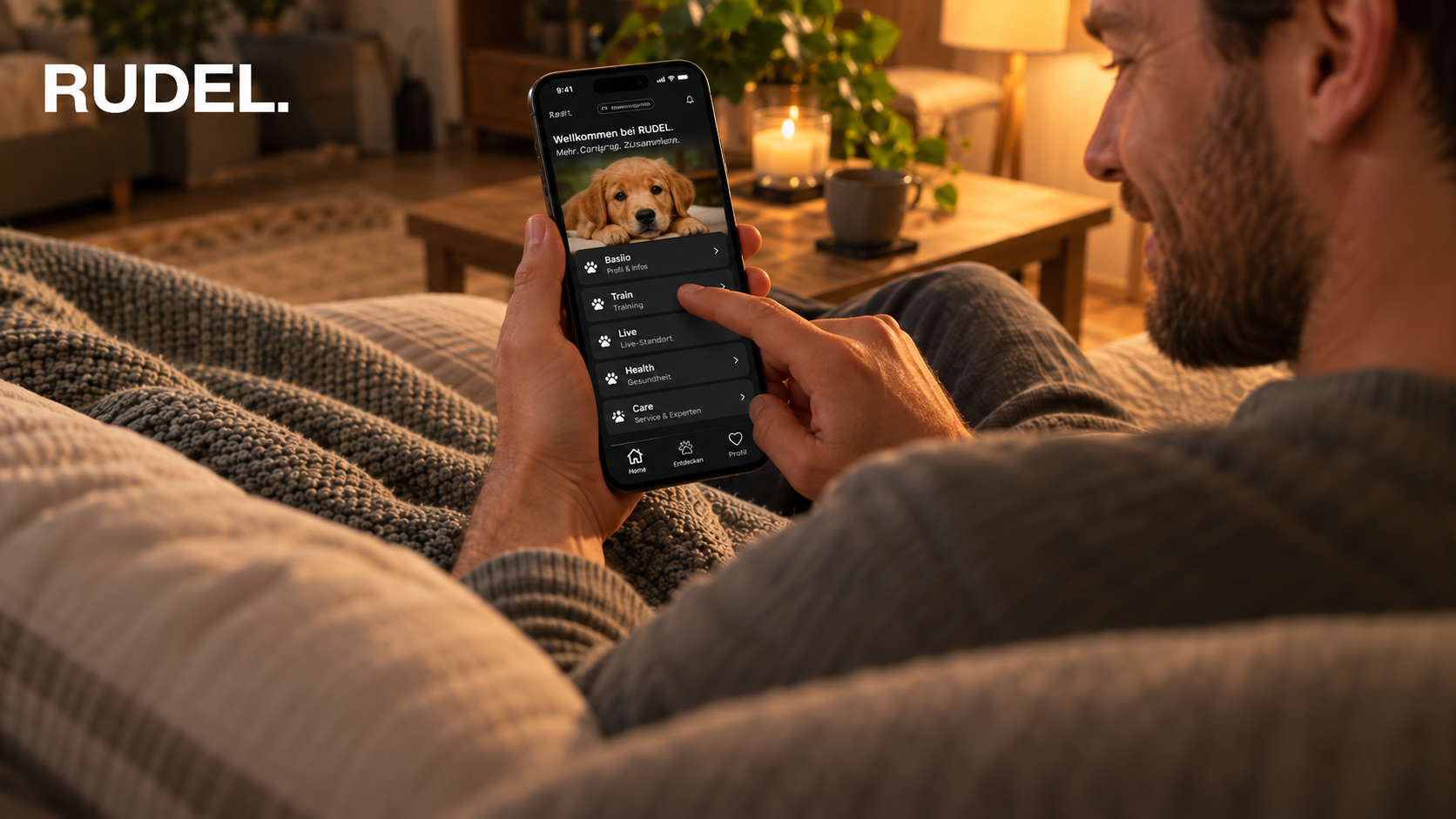 Ein Mann liegt entspannt auf dem Sofa im warmen Abendlicht und schaut auf sein Smartphone, auf dem die Startseite der RUDEL App mit einem Welpenfoto und verschiedenen Kategorien zu sehen ist